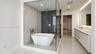 Glass-enclosed wet room featuring a freestanding soaking tub, dual-tone tile surround, and brushed gold fixtures, complemented by a dual-sink vanity w