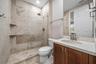 Full vanity with wood-finish cabinetry, under-mount sink, and dual-handle faucet with travertine marble floor to ceiling and modern frameless glass sh
