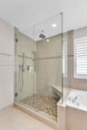 Walk-in shower featuring a frameless glass enclosure, rainfall showerhead, handheld sprayer, built-in corner bench, and mosaic tile flooring with deco