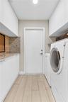 Utility room featuring wood-finish flooring, white flat-panel upper and lower cabinetry, stone-finish countertops, and a decorative mosaic tile backsp