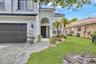 Stucco exterior featuring an arched entryway, paver driveway, dark-toned garage door, and a manicured lawn with mature palm landscaping