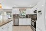 Kitchen featuring white cabinetry, stone countertops, stainless steel appliances, multi-tonal mosaic tile backsplash, and wood-finish flooring