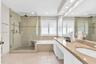 Bathroom featuring a dual-sink vanity with stone countertops, a glass-enclosed walk-in shower with a tiled bench and pebble-style flooring, a deep soa
