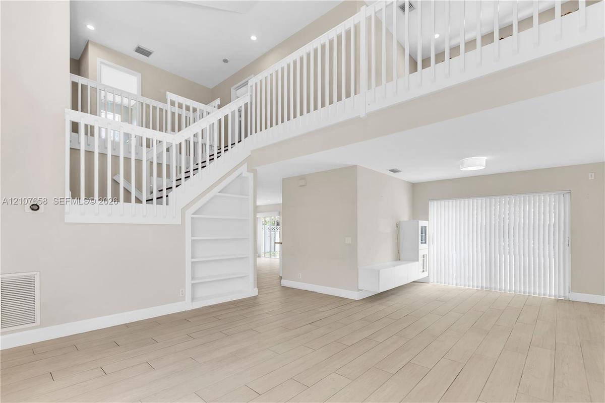 Two-story foyer with a mezzanine balcony, wood-finish flooring, white staircase featuring open shelving, and a wall-mounted floating storage unit