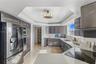 Kitchen featuring dark-toned cabinetry, solid-surface countertops, stainless steel appliances, tray ceiling with recessed lighting, and stone flooring