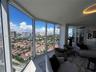 Floor-to-ceiling windows featuring panoramic urban and coastal scenery, neutral tile flooring, and integrated recessed ceiling lighting