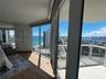 Floor-to-ceiling glass windows, expansive private balcony with glass railing, wood-finish flooring, and direct coastal and city panoramas