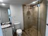 Bathroom featuring a walk-in shower with glass enclosure, tiled surround, and overhead rainfall fixture, complemented by a vanity with a stone counter