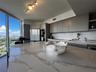 Kitchen featuring an oversized island with a stone-finish countertop, flat-panel cabinetry, integrated wall ovens, and floor-to-ceiling windows