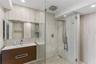 Wall-to-wall stone tile, glass-enclosed shower featuring a rainfall showerhead and integrated body sprays, floating wood-finish vanity, and integrated
