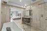 Full-height stone-tiled walls, freestanding soaking tub, glass-enclosed walk-in shower with rainfall fixture, recessed shower niche, and wall-mounted 
