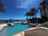 Swimming pool with stone-tile decking, metal handrails, and surrounding mature palm trees