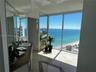 Floor-to-ceiling windows, stone tile flooring with decorative inlay, expansive vanity with integrated sink, and full-wall mirrors overlooking the ocea