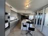 Contemporary kitchen featuring flat-panel cabinetry, a waterfall-edge stone island, built-in stainless steel appliances, stone flooring, and expansive