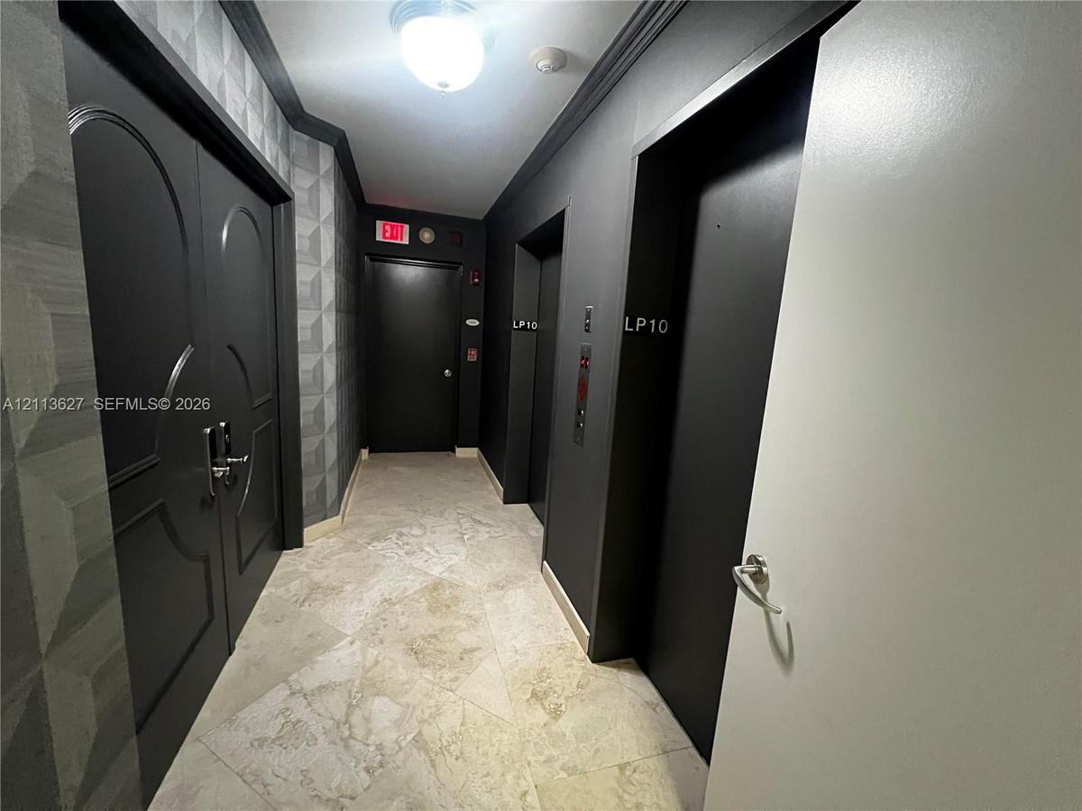 Stone tile flooring, geometric textured wall covering, double-door entry with metallic hardware, dual elevator access, and monochromatic architectural