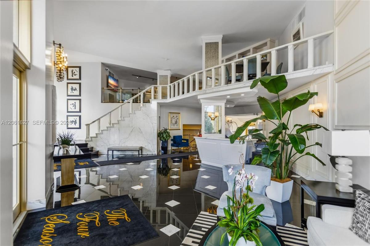 Double-height foyer featuring polished stone flooring with inset diamond pattern, stone-clad staircase, mezzanine level with decorative balustrade, an