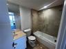 Bathroom featuring a stone-topped vanity with an undermount sink, a large wall-mounted mirror, and a tile-surround tub with a glass panel enclosure