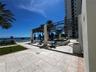 Outdoor terrace featuring stone tile flooring, a structured metal pergola, swimming pool, manicured lawn, and ocean backdrop