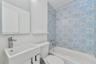 Bathroom featuring a vanity with a rectangular basin, metallic faucet, wall-mounted mirror, and a shower-tub combination accented with patterned tile 