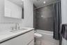 Bathroom featuring a floating vanity with a stone-top integrated sink, chrome widespread faucet, frameless wall-mounted mirror, and a shower-tub combi