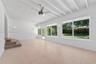 Open-concept space featuring expansive floor-to-ceiling windows, high exposed-beam ceilings, large-format tile flooring, and a central ceiling fan