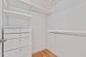 Walk-in closet featuring white built-in drawers, adjustable shelving, metal hanging rods, and wood-finish flooring