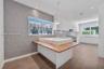 Kitchen featuring matte white flat-panel cabinetry, hexagonal-patterned accent wall, stone-topped island with wood-finished breakfast bar, and tile fl