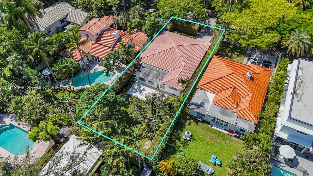 Aerial perspective of a property featuring a hip roof, concrete patio, mature landscape, and perimeter privacy hedging
