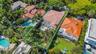 Aerial perspective of a property featuring a hip roof, concrete patio, mature landscape, and perimeter privacy hedging