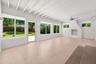 Exposed beam vaulted ceiling, white-painted brick fireplace, large-format tile flooring, oversized windows, and glass-paneled exterior door