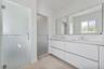 Bathroom featuring a dual-sink floating vanity with white cabinetry, a full-width wall mirror, oversized tile flooring, and frosted glass door enclosu