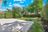 Concrete paved patio featuring a grass lawn, mature trees, and perimeter shrubbery