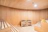 Sauna featuring wood-paneled walls and ceiling, tiered slatted wood benches, and dual built-in heating units