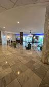 Polished stone flooring throughout, expansive wall-to-wall stone cladding, central chandelier, and decorative metal balustrade with a wooden handrail