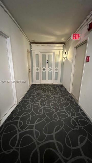 Hallway featuring patterned carpeting, paneled wood door with decorative molding, and wall-mounted sconce lighting