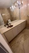 Bathroom vanity with a stone countertop, integrated oval sink, multi-drawer cabinetry, full-wall mirror, and dual crystal chandeliers