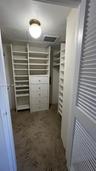 Walk-in closet featuring built-in shelving, a central five-drawer dresser, patterned carpeting, and a louvered door
