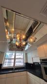 Tray ceiling featuring a recessed mirrored panel, multi-tiered chandelier with decorative glass shades, solid surface countertops, and white cabinetry