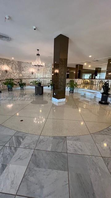 Grand foyer featuring polished stone flooring, custom-patterned wall finishes, a central structural column with a reflective finish, a multi-tiered cr