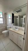 Bathroom featuring a white vanity cabinet with stone-finish countertop, oval undermount sink, expansive wall-to-wall mirror, and light-tone tile floor