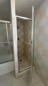 Walk-in shower enclosure featuring a chrome-framed hinged door, wall-mounted shower head, integrated towel bar, and checkerboard-patterned tile wall s