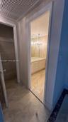 Storage closet featuring wire shelving and stone-finish tile flooring, leading to a bathroom with a vanity, stone-finish countertop, and decorative ch