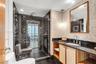 Bathroom featuring a pebble-stone accent wall, custom wood-finish vanity with a dark countertop, glass-enclosed shower with black diamond-patterned ti