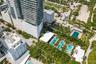 High-rise residential structure featuring glass-paneled balconies, multiple swimming pools, extensive lush landscaping with mature palm trees, and har