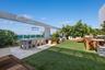 Rooftop terrace featuring synthetic lawn, wood-decking accents, stone-tile flooring, glass panel railing, and overhead structural beam with integrated