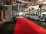 Industrial fitness space featuring exposed ceiling infrastructure, rubberized flooring, a centered synthetic turf track, and full-wall mirrors