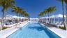 Linear swimming pool featuring white tile decking, stainless steel entry rails, perimeter palm trees, and ocean horizon backdrop