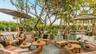 Outdoor lounge area featuring wood decking, sand surfacing, natural-finish wood elements, mature trees, and fixed thatched-roof structures