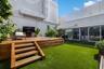 Outdoor courtyard featuring a multi-level wood deck, built-in recessed fire feature, synthetic lawn, and perimeter privacy fencing