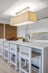 Kitchen island featuring a waterfall-edge countertop, stone-tiled base, undermount sink with a gooseneck faucet, white flat-panel cabinetry, and a rec